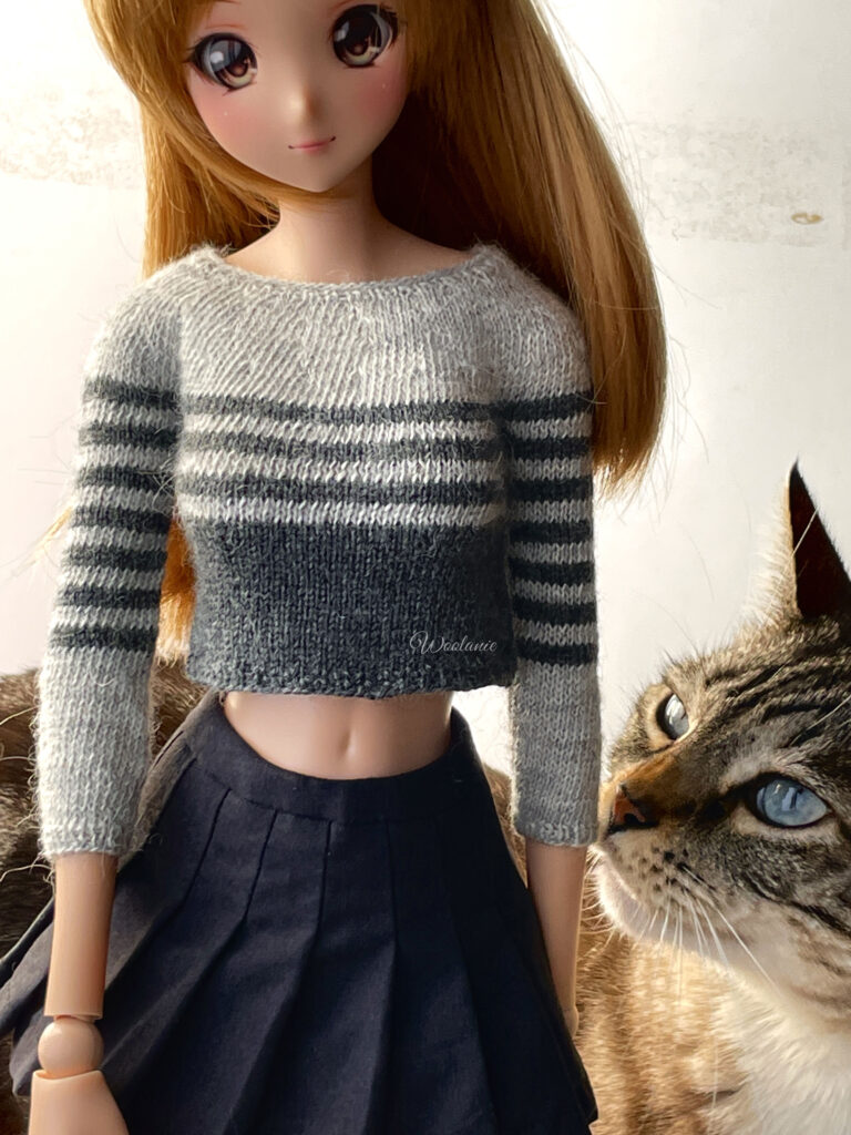 Jersey tejido a mano en alpaca gris con rayas, puesto en SmartDoll con gato de fondo.