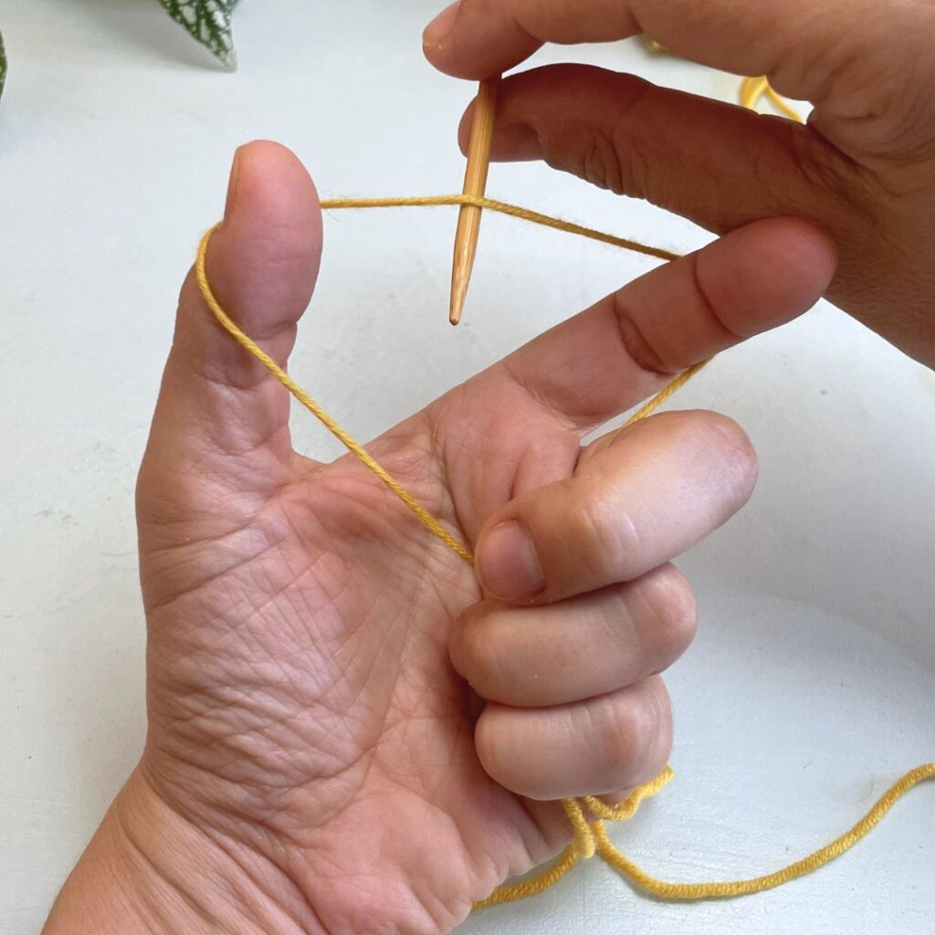Sujeta la aguja tras la hebra que queda entre los dedos pulgar e índice