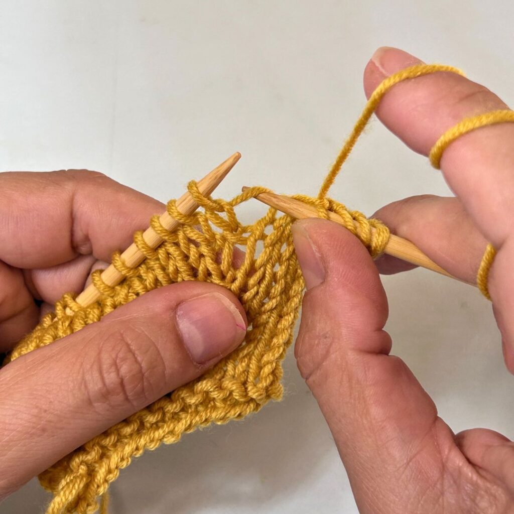 Lo primero para hacer un aumento en punto a dos agujas es localizar la hebra que une dos puntos. Introduce la aguja derecha por debajo de esa hebra