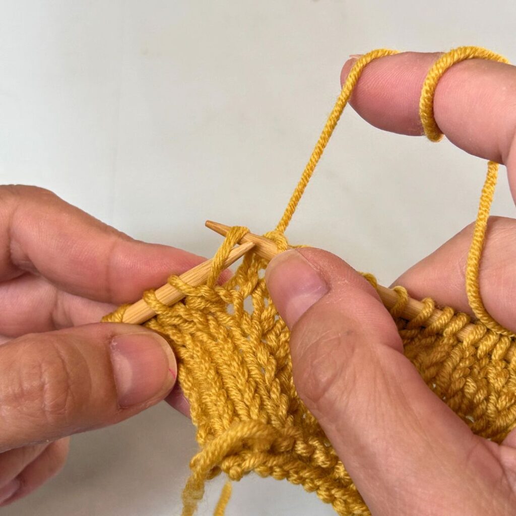 Coloca la hebra levantada en la aguja izquierda, con la pata izquierda por delante de la aguja